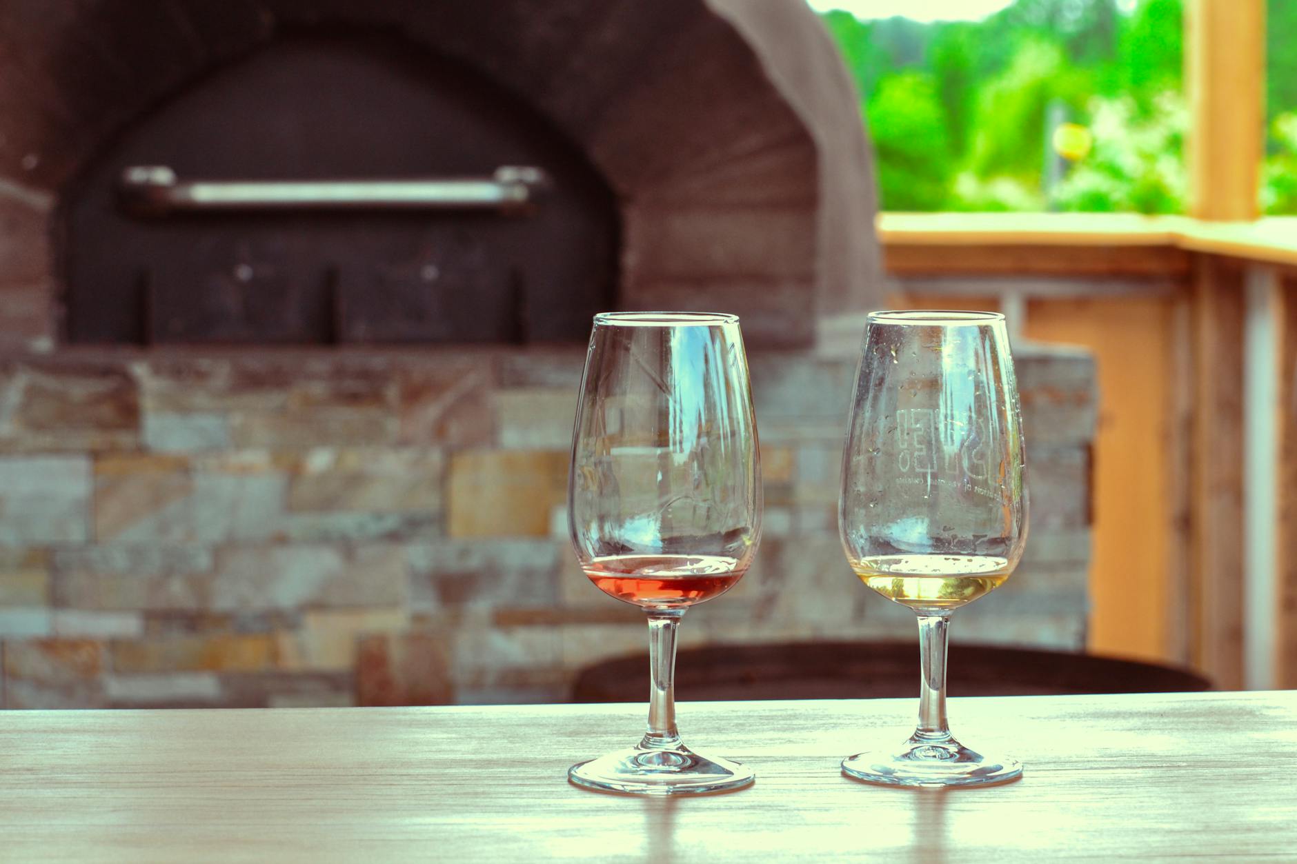 Dwa puste kieliszki na stole w ogrodzie z kamiennym piecem w tle
